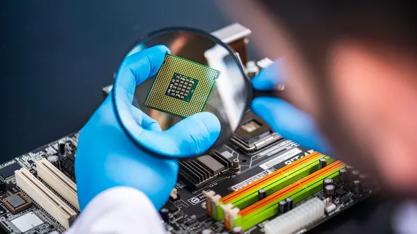 A person wearing blue latex gloves holding a magnifying glass over a microchip.