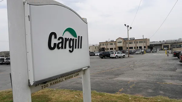 A sign reading "Cargill" is seen at the entrance of a parking lot to a factory building