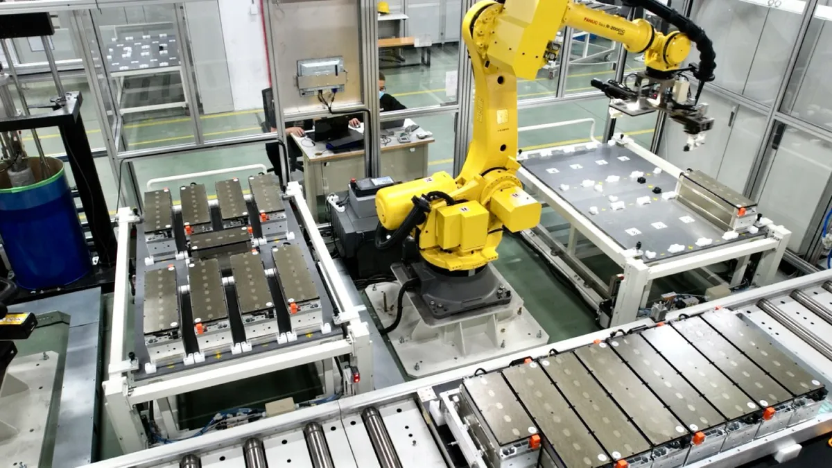 A yellow robot working on a silver battery cell in a facility.