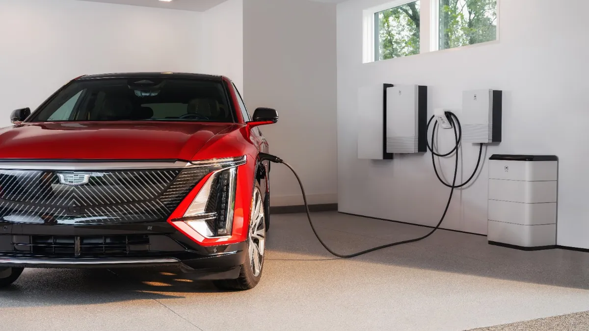 A red Cadillac Lyriq in a garage plugged into a GM Energy residential charger.