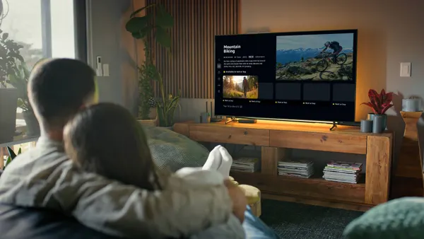 A rendering of a couple sitting on a couch in daytime watching a flatscreen TV