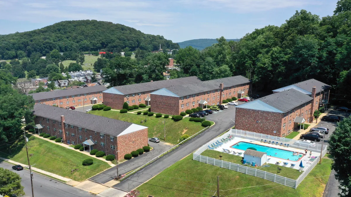 Aerial picture of brick apartments, grass, parking lots and a pool.