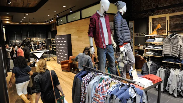 The interior of a Timberland store. Mannequins wearing Timberland clothes stand on a table display as customers walk around it.