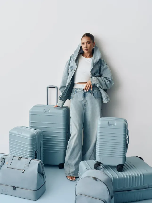 A model wears clothing from the Gap/Beis collection in front of luggage from the collection.