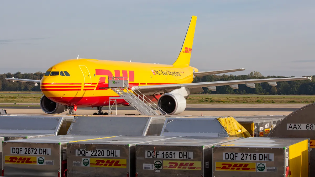 A DHL aircraft on a tarmac with branded cargo boxes in the forefront