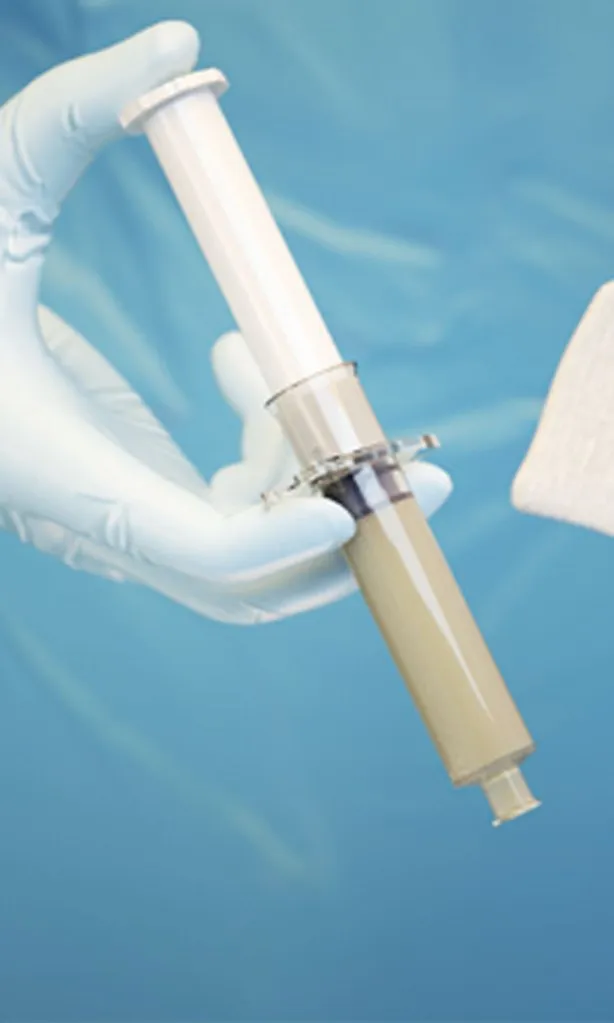 A syringe filled with a hummus-colored gel against a blue background.