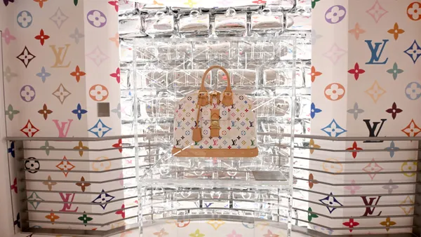 A colorful Louis Vuitton handbag sits in a clear display case.