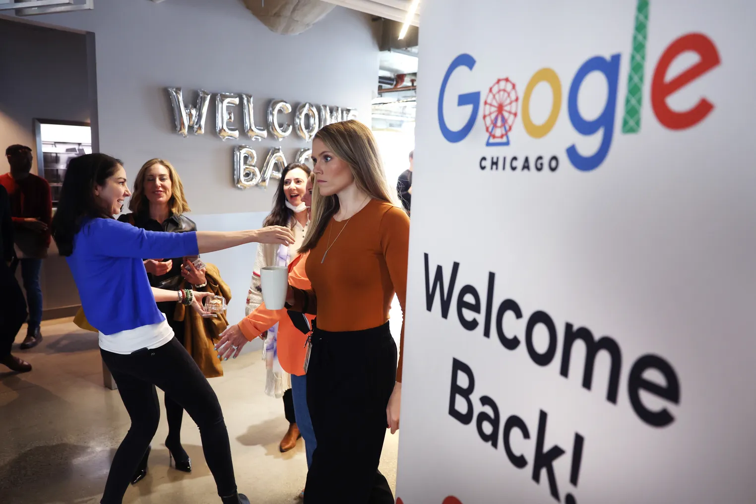 Google employees stand in a hallway greeting each other near a "Welcome back" sign.