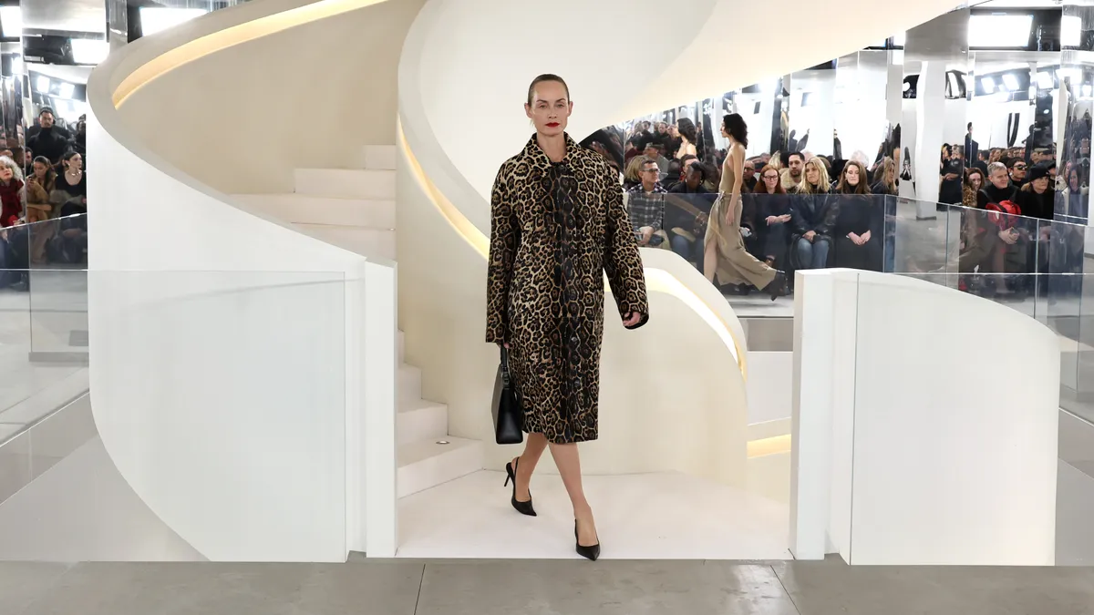 A model in a leopard print coat comes down a white spiral staircase.