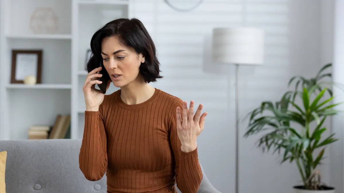 Frustrated person talks on mobile phone, sitting on sofa at home.