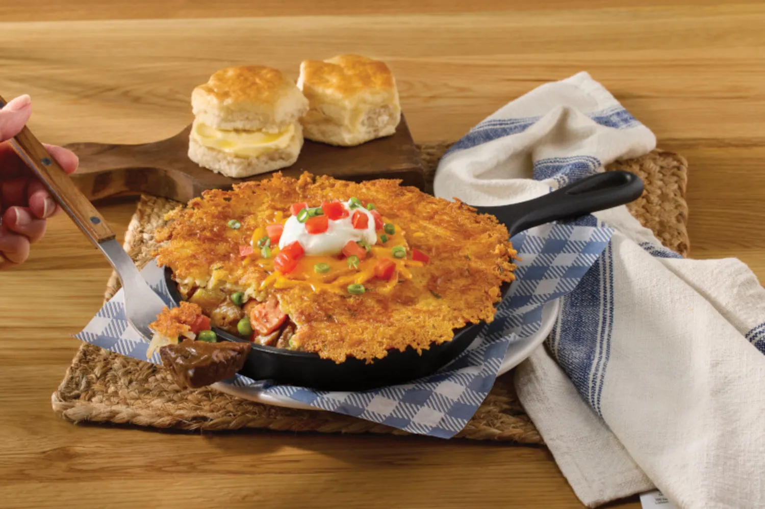 An image of a Hashbrown Shepherd's Pie offered in a cast iron skillet. A hand with a fork has beef at the end.