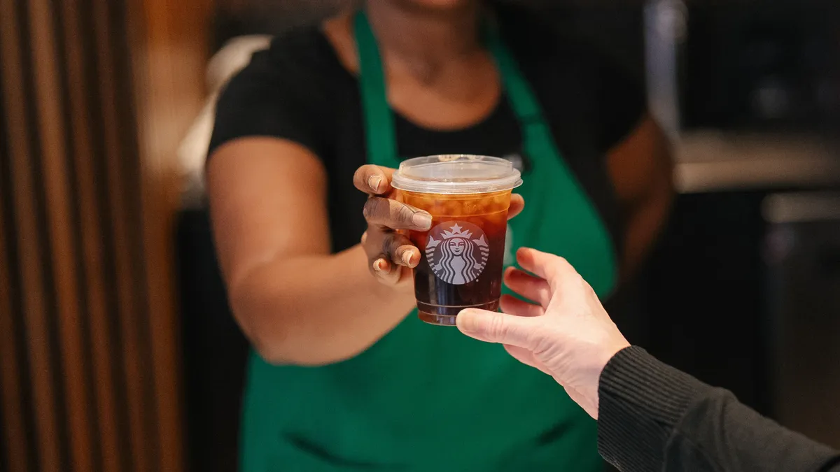 A Starbucks barista hands a customer a coffee