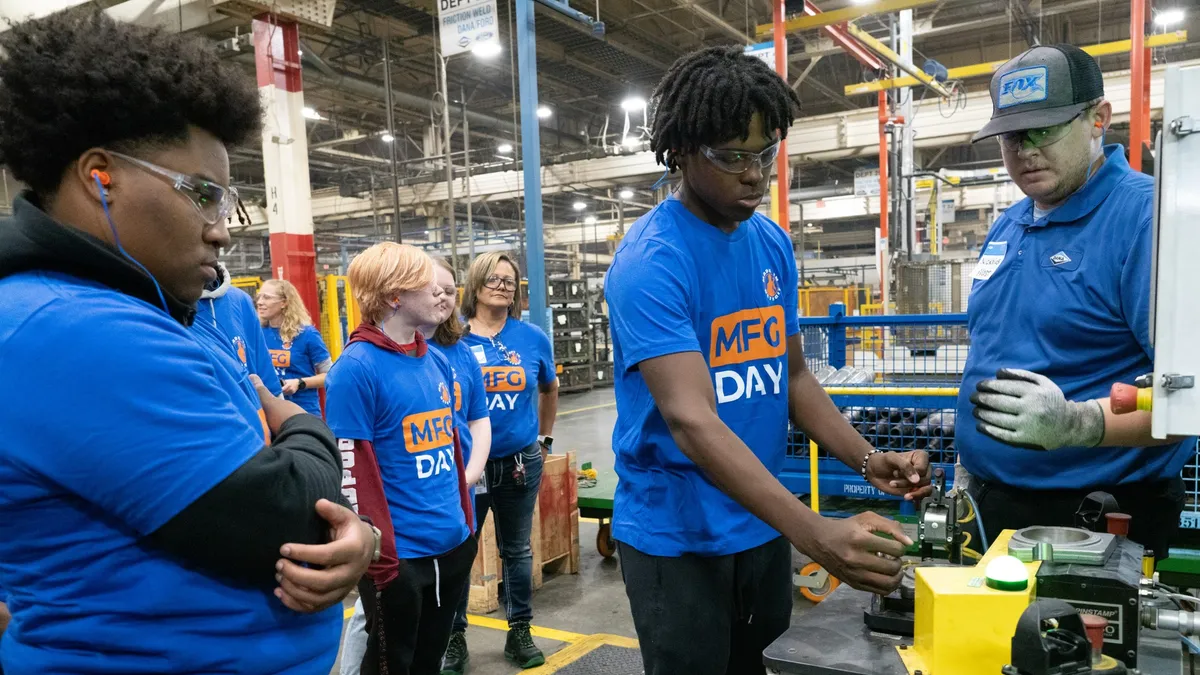 A student takes a turn testing manufacturing equipment while others observe.