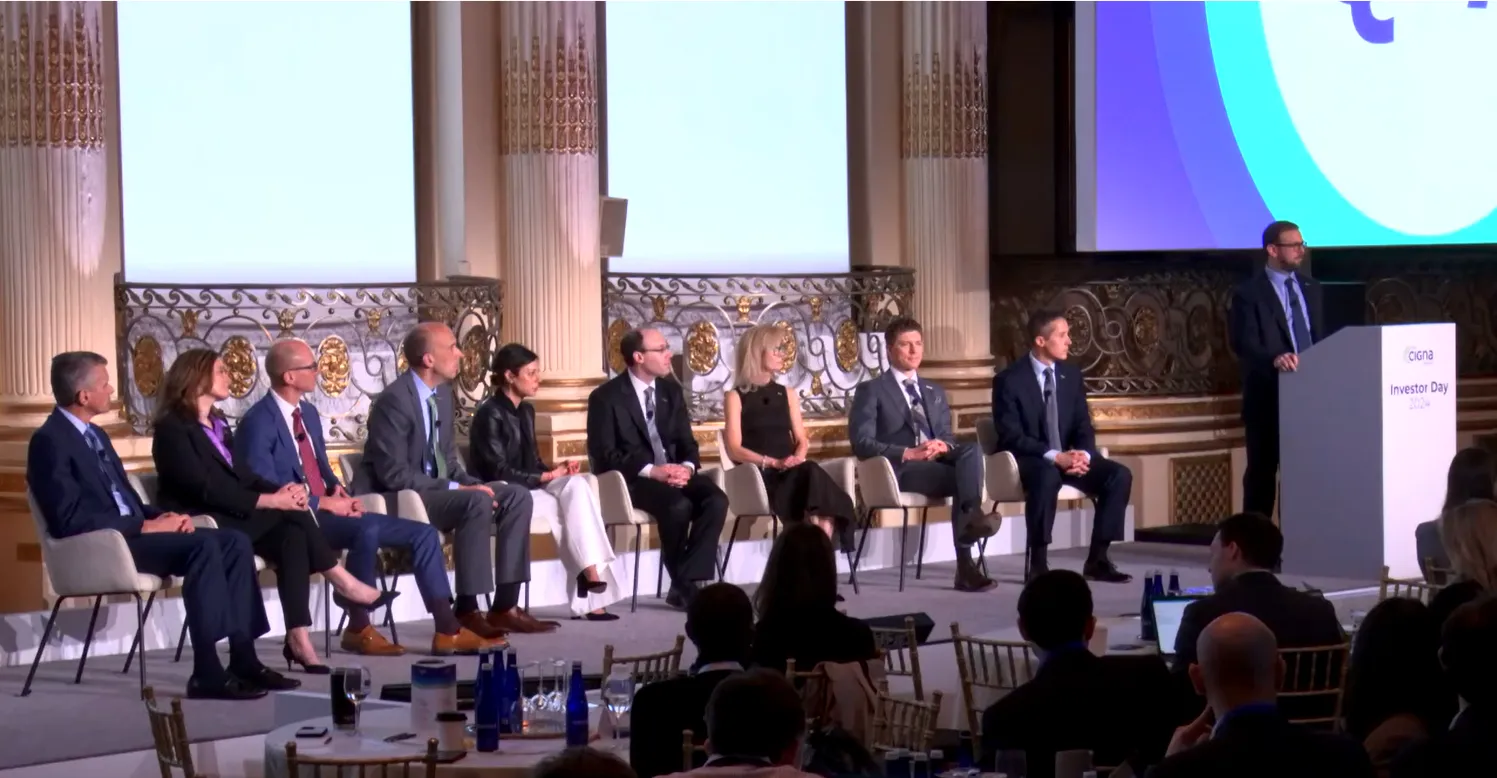 A line of executives sit on a stage.