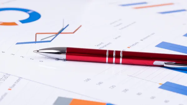 Red pen on papers with financial spreadsheets and graphs.