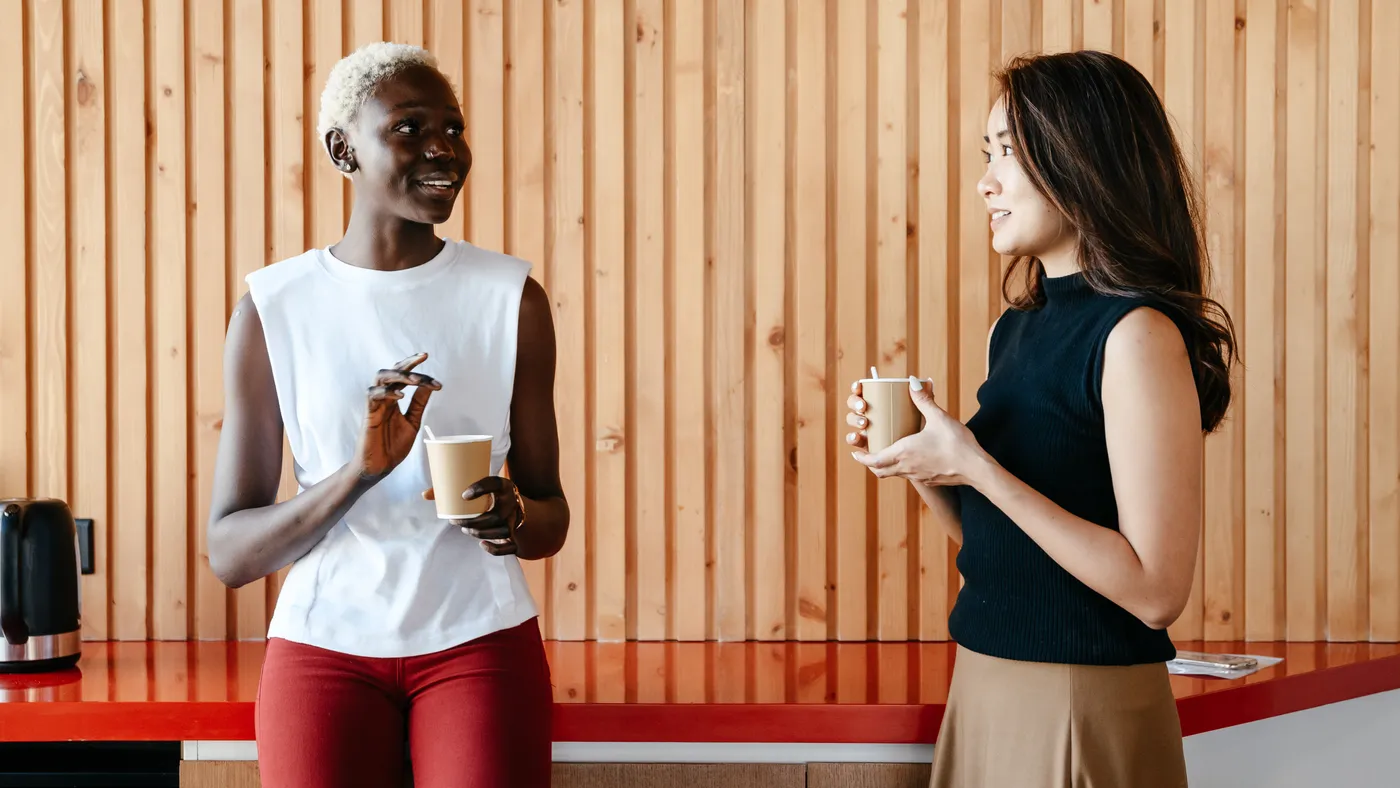 An Asian person and a Black person talk in the office