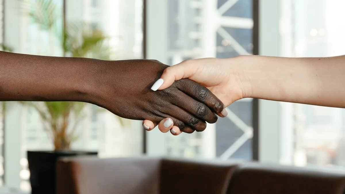 A dark brown hand shakes a pale white hand