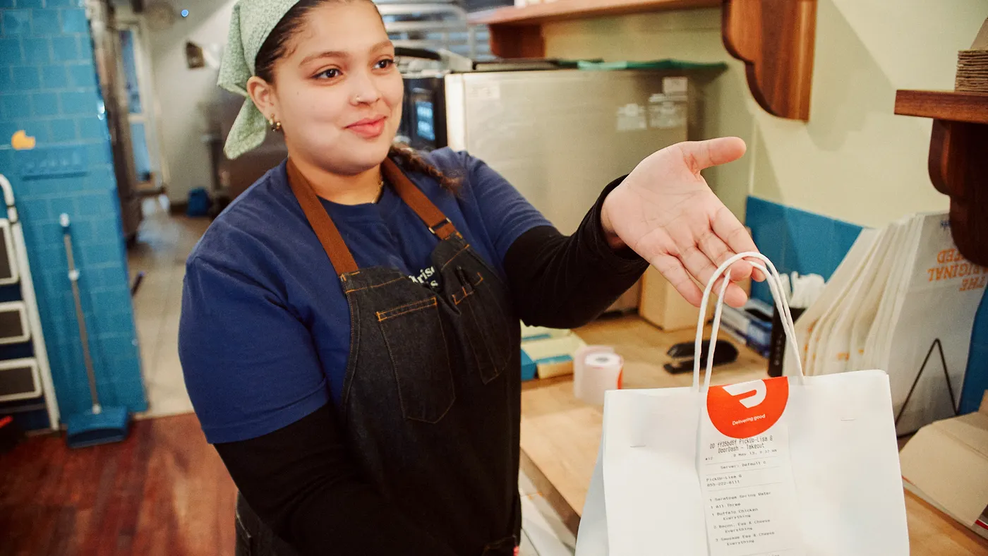 Woman handing over a bag sealed with a DoorDash sticker