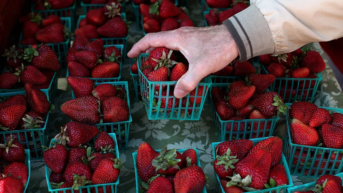 A close up of a hand picking up a basket of strawberries in a farmers market display