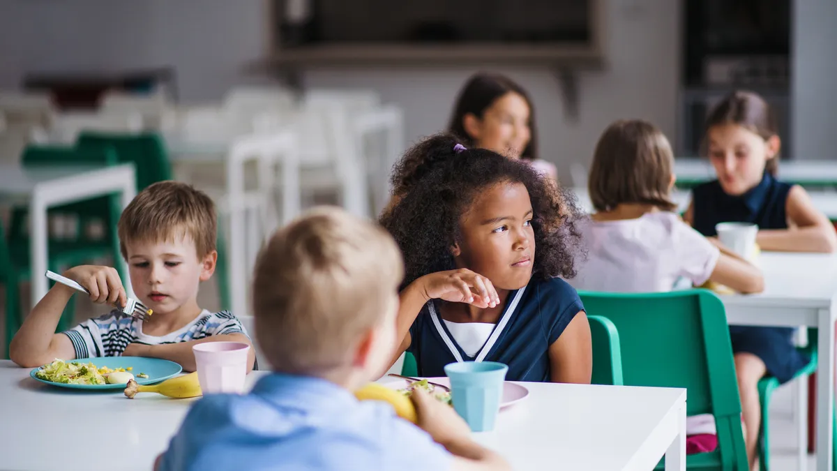 A group of young students sit and eat together in the school cafeteria.