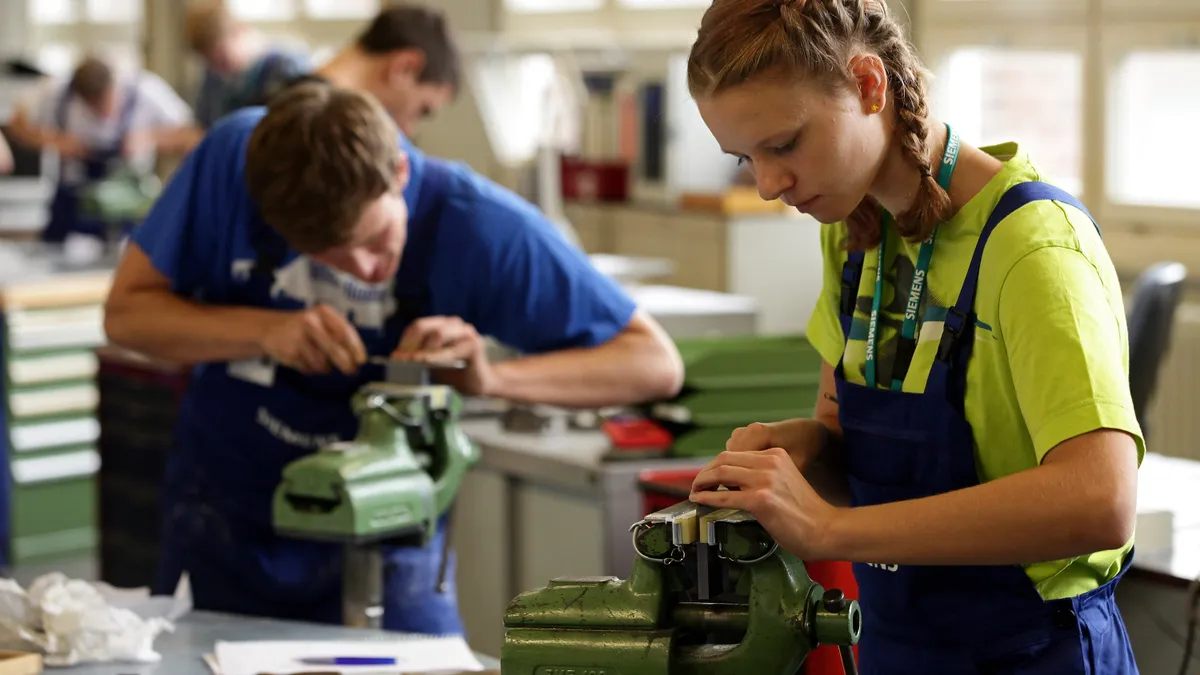 A young woman and man are shown learning how to use precision filing machinery during a training session for Siemens.