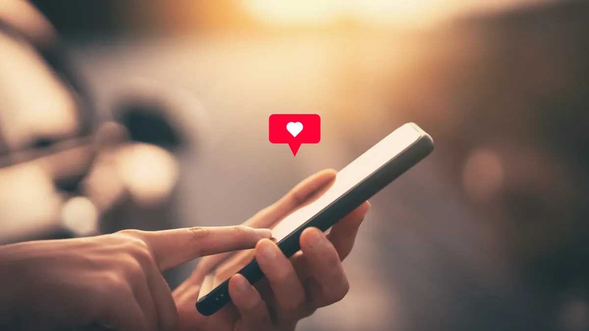 Close up of a woman's hand holding a smart phone with a heart icon.