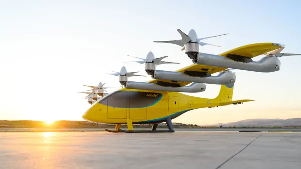 A small yellow aircraft with six propellers parked on an airport apron.