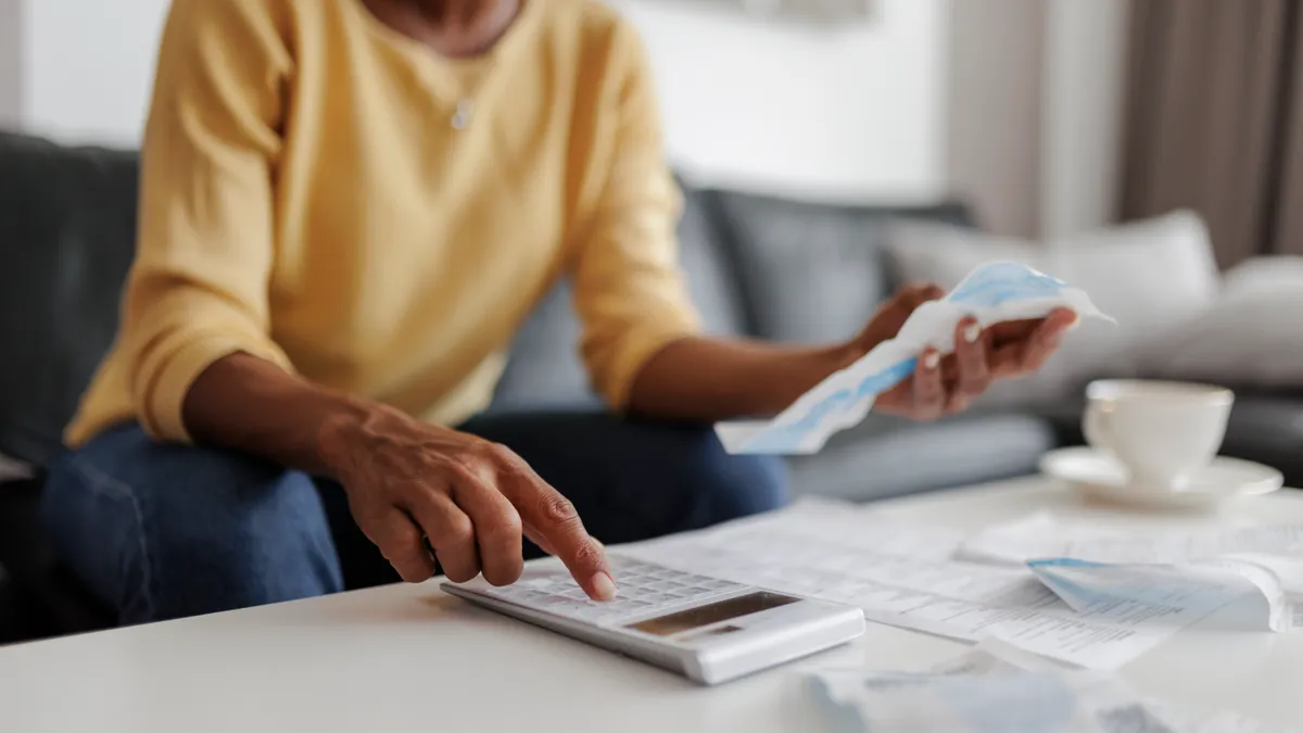 Close up of a person with a calculator and holding a bill.