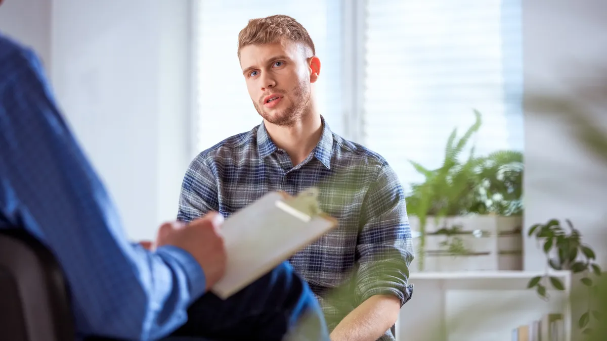 A young white man in a plaid shirt talks to a therapist who is just out of frame.