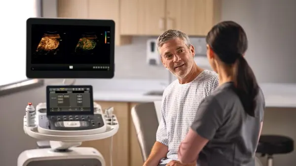 Two people talk while a screen displays a medical image.