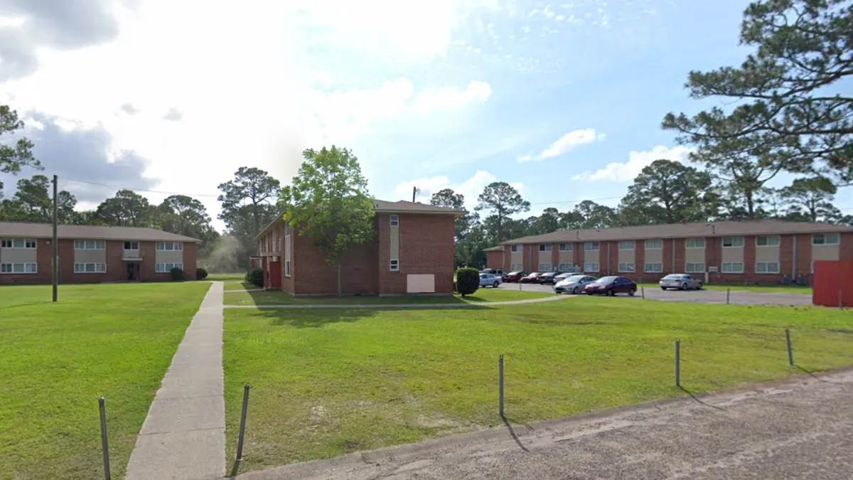 A group of low-rise apartment buildings situated on a green lawn on a sunny day.