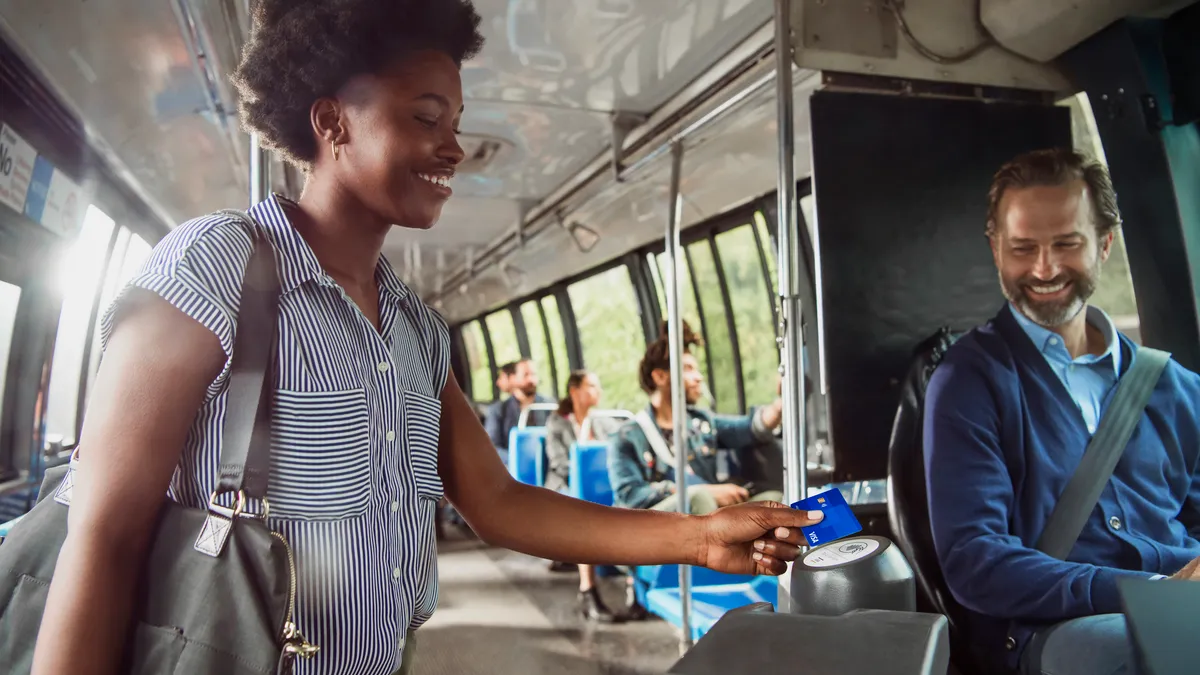 A woman on a bus using her Visa card as payment as the bus driver smiles and looks on.