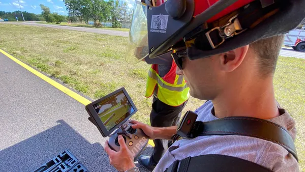 A person wearing a helmet on a runway holdiing a handset with the word "Viper" and a screen.