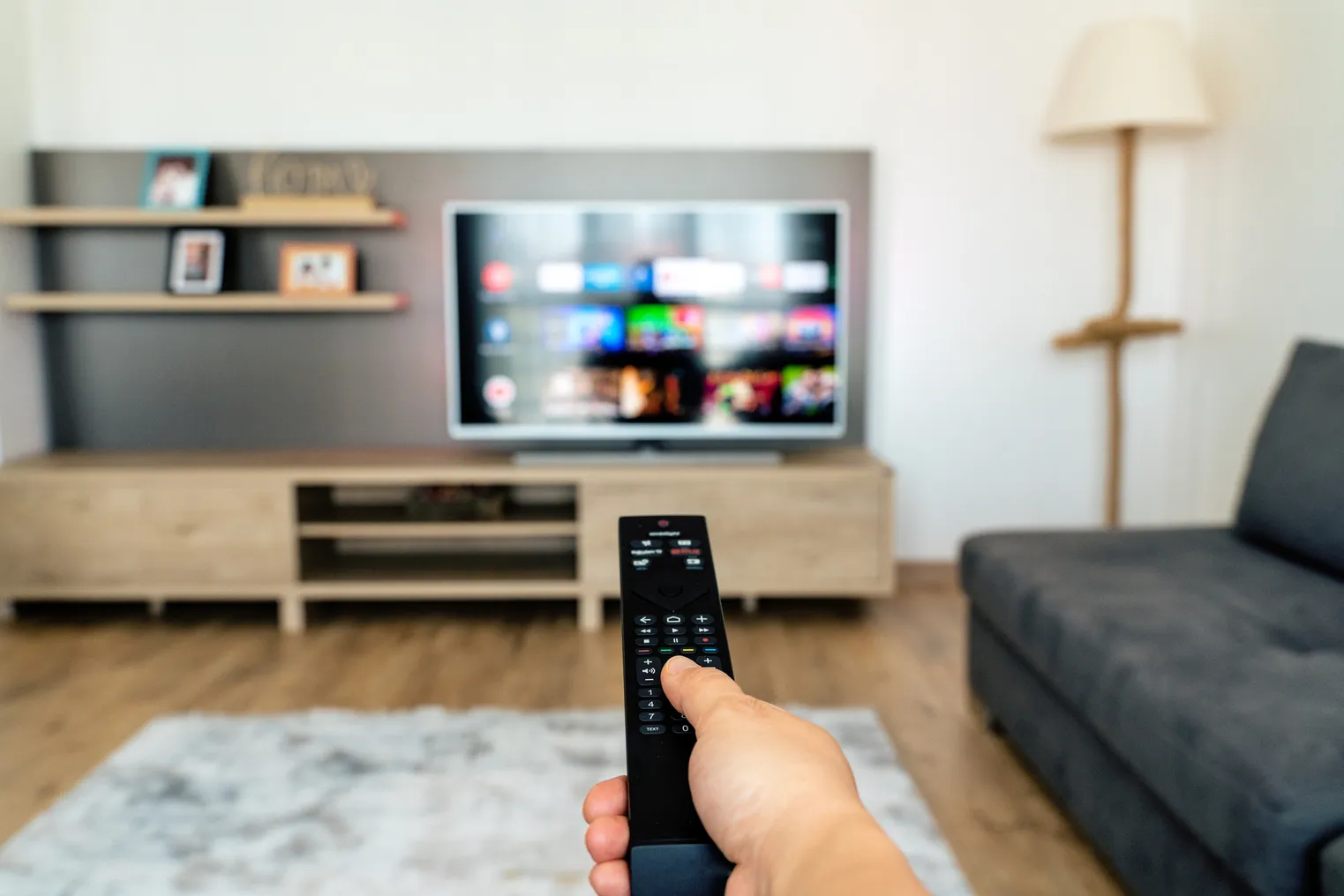 A hand holds up a remote in front of a television screen.