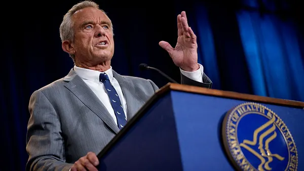 Robert F. Kennedy Jr. stands in front of a podium, speaking with a hand raised.