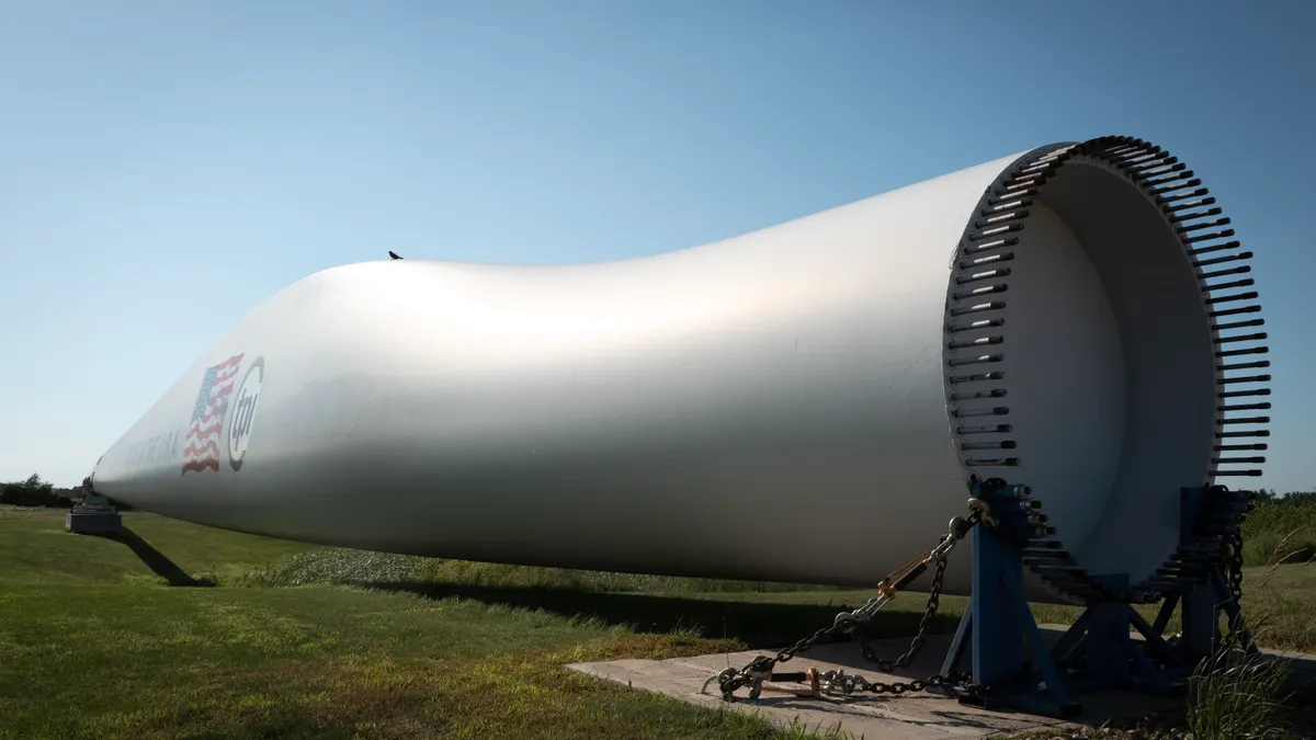 A composite wind blade, used in the construction of power-generating wind turbines, is displayed in front of a manufacturing facility.