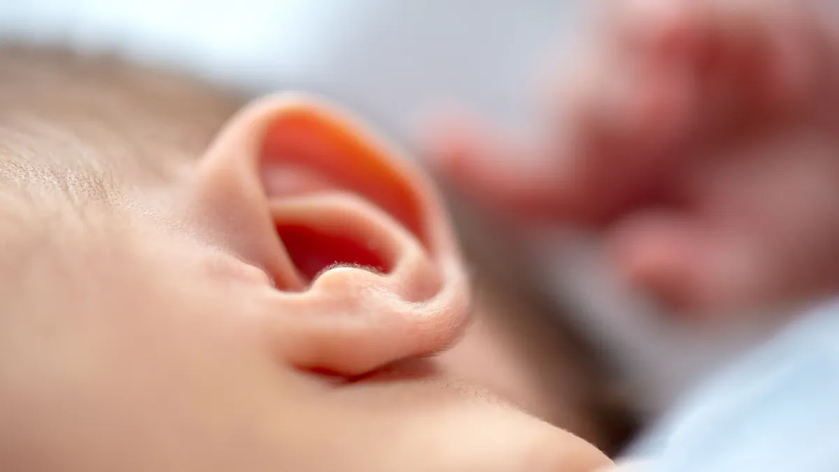 An infant's left ear is in the foreground of this image, which is otherwise blurred.