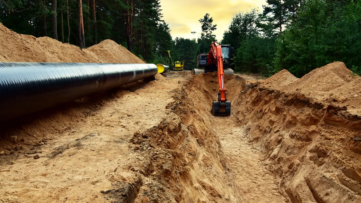 Excavator digs trench at forest area sunset background.