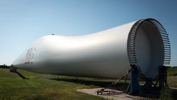 A composite wind blade, used in the construction of power-generating wind turbines, is displayed in front of a manufacturing facility.