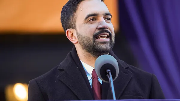 A closeup of a man in a suit and tie speaking into a microphone on a stage.