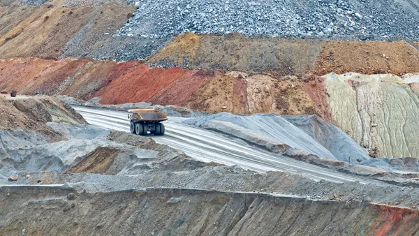A yellow truck carries ore across a road in an open pit.