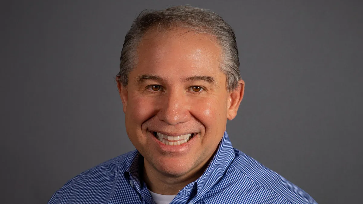 A portrait photo of Whataburger CEO Ed Nelson, a man with gray hair, smiling, while wearing a blue checked button down