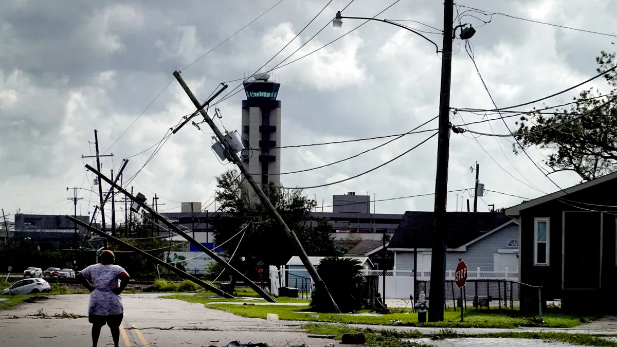 A woman stands in the road surrounded by downed power lines and debris