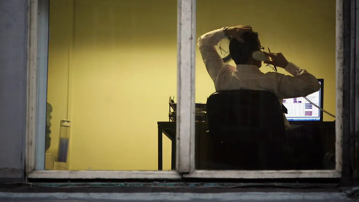 An office worker is seen from behind as he sits at his desk.