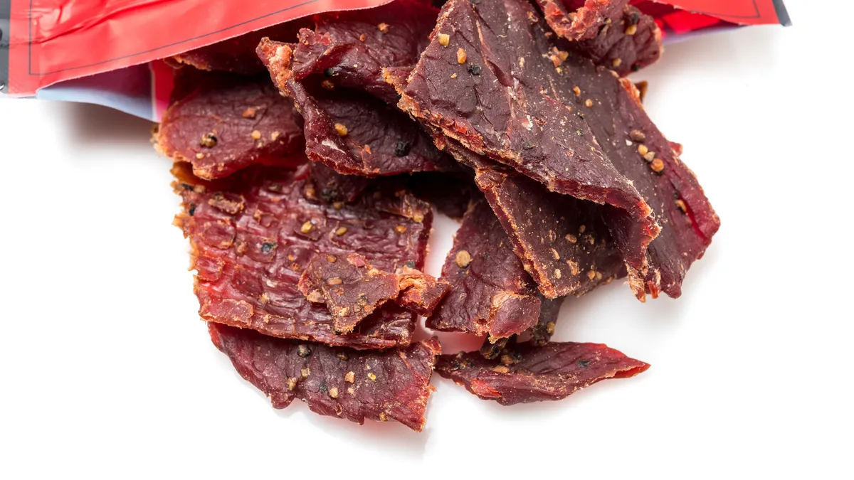 Beef jerky close up coming out of a bag on white from above