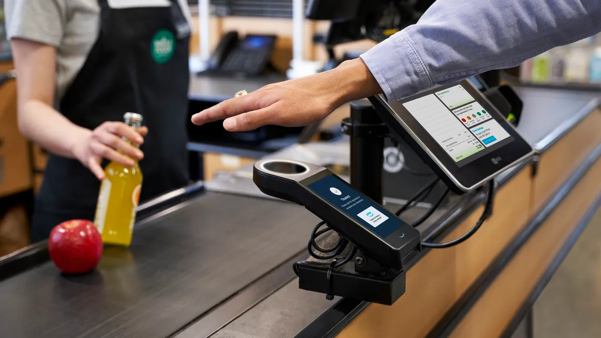 Individual holding its hand under Amazon One's palm recognition payment method at a Whole Foods Market checkout counter