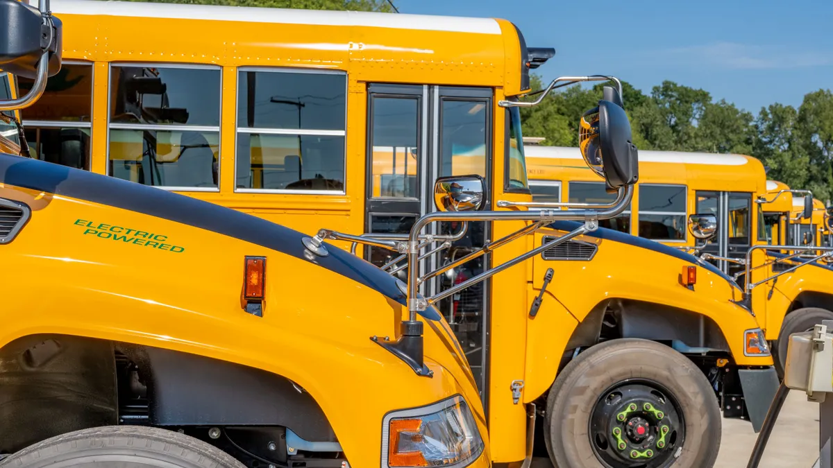 A row of yellow electric school buses charging next to each other.