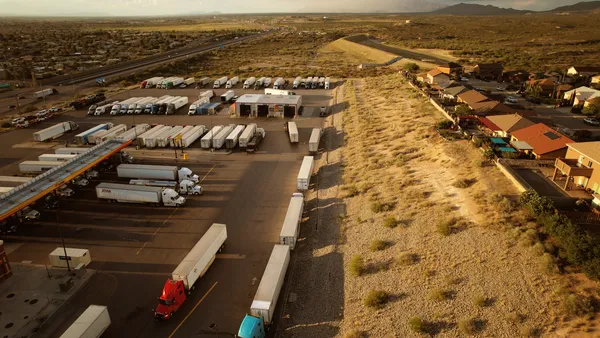 A desert landscape surrounds a truck stop near homes and a mountain range on the horizon.