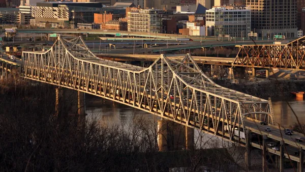 View of a double decker bridge over a river with a city skyline in the background.