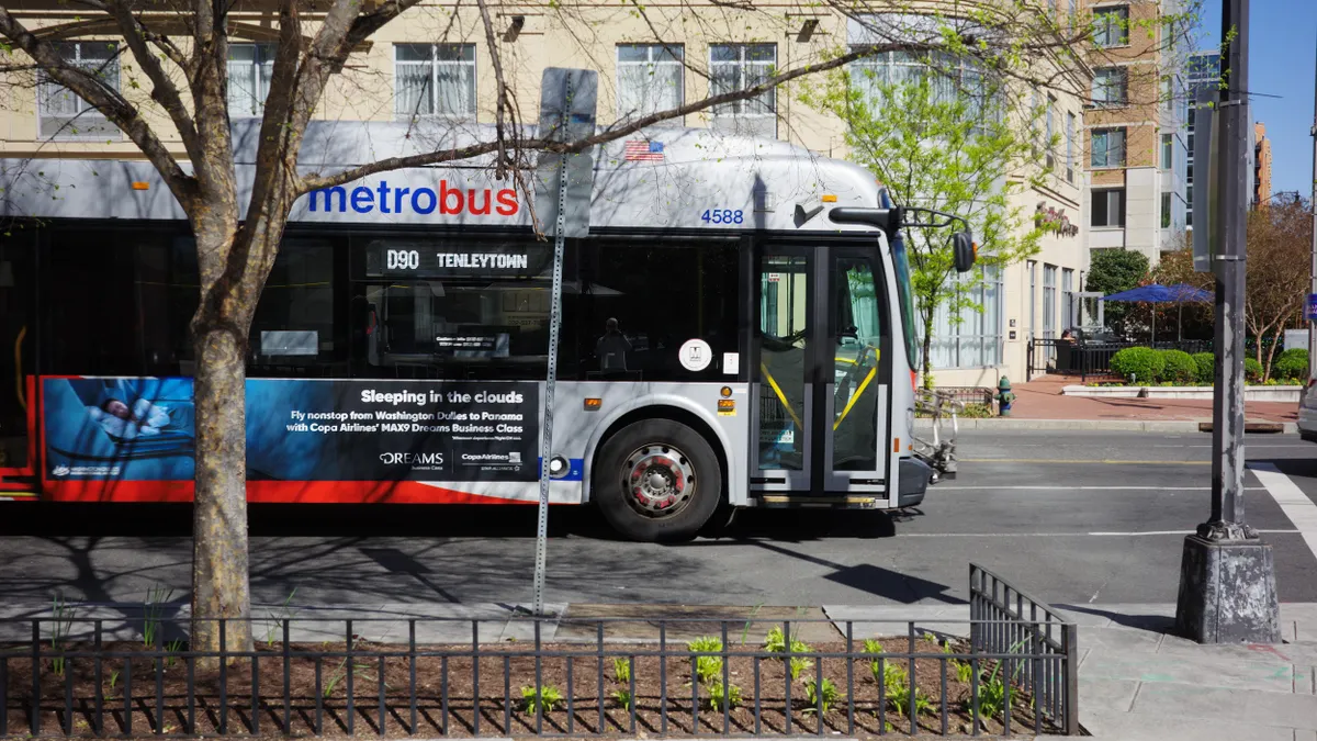 Side view of a transit bus lettered "metrobus" on a street with buildings behind it.